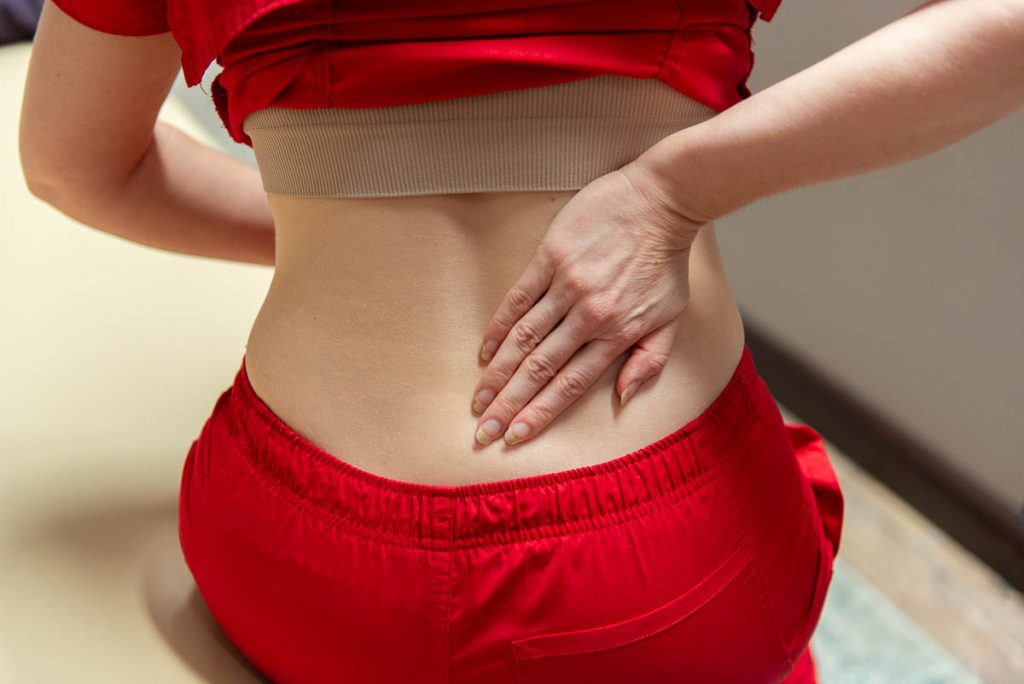 Woman holding back in pain on examination table.